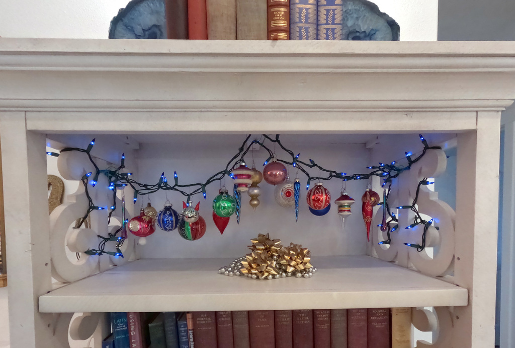 Bookshelf decorated with 20 ornaments hanging from a string of little blue lights